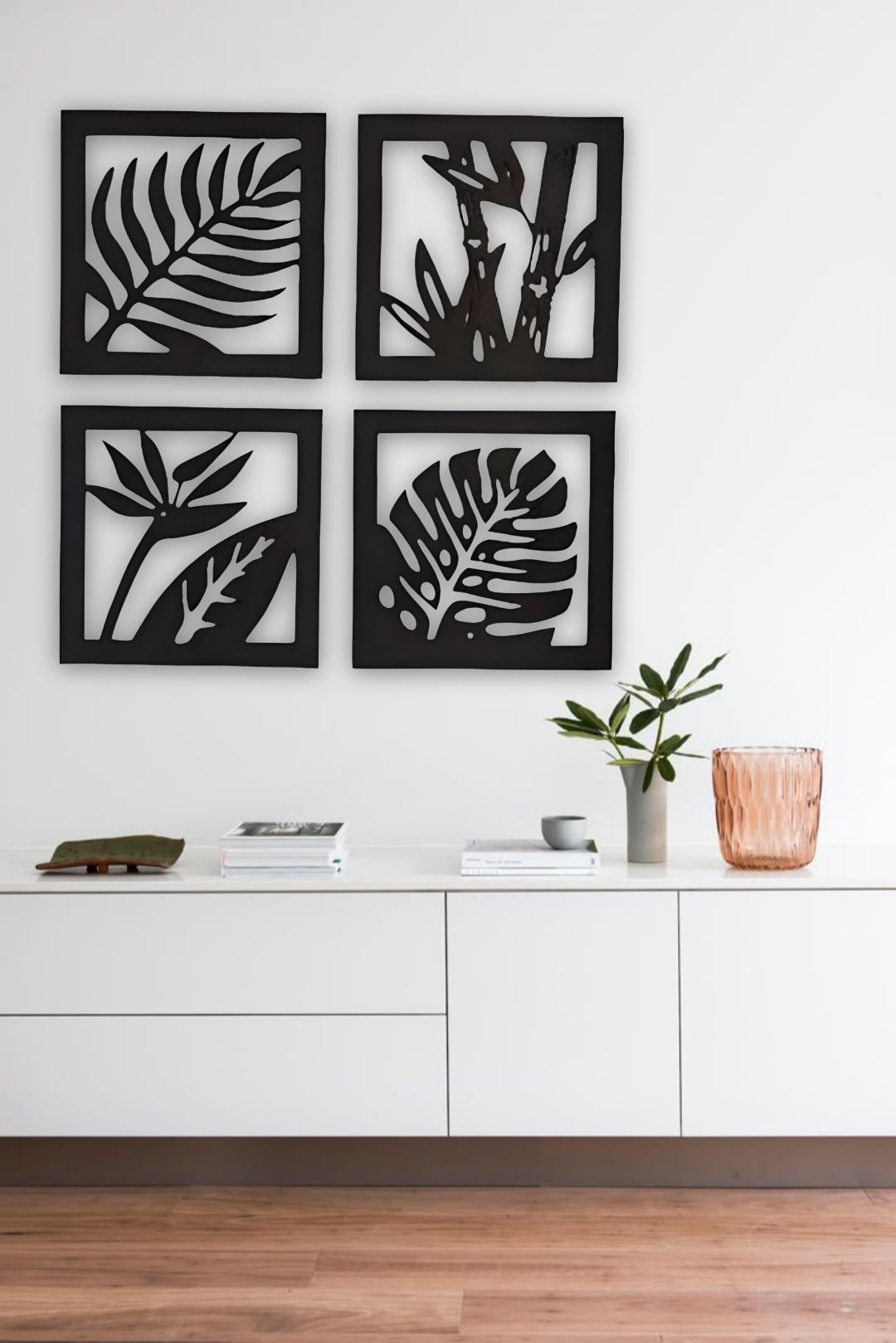 “Four-piece square wooden wall art set with tropical leaf and plant designs in black finish, mounted above a modern wooden sideboard.”