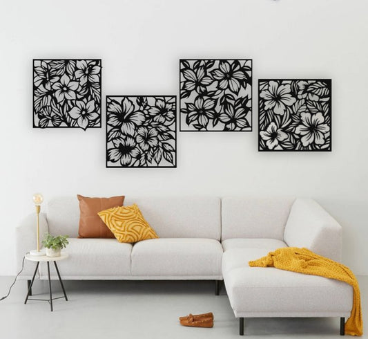 "Modern living room with a white L-shaped sofa and yellow accents, featuring a set of four black wooden laser cut floral wall art panels mounted on a white wall. Each panel displays intricate flower and leaf patterns, arranged in a staggered layout above the couch."