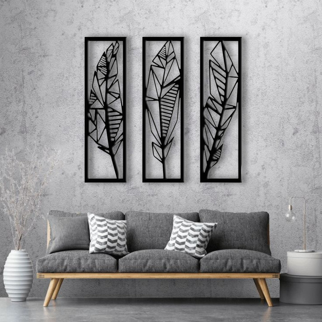 Modern black wooden wall art featuring a set of three vertical panels with abstract geometric feather designs, mounted on a light grey textured wall above a grey sofa.