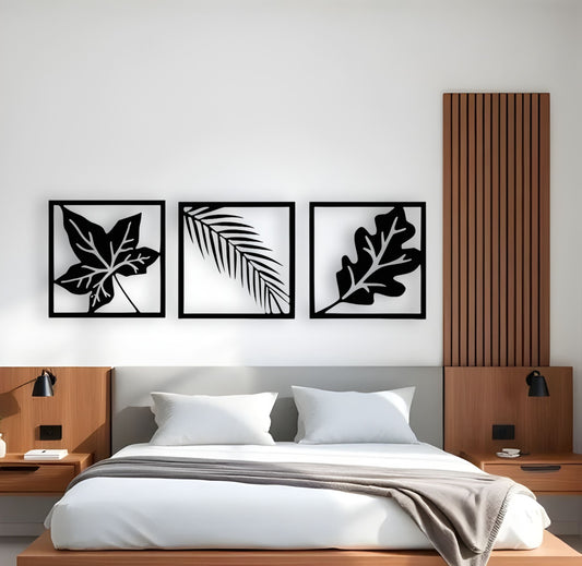 Modern wooden wall art in black featuring three framed botanical leaf designs mounted above a bed in a minimalist bedroom interior.