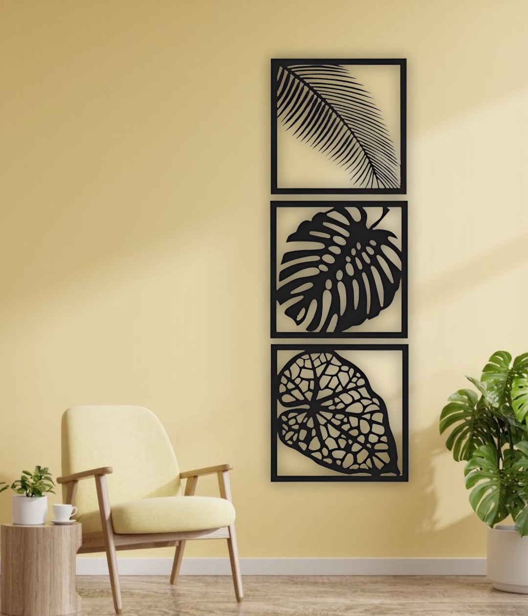 Three-piece vertical black wooden wall art set with palm, monstera, and vine leaf designs, mounted beside a cream sofa on a white wall.