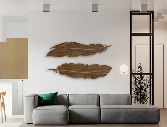 Two horizontal feather-shaped wooden wall decor pieces in brown finish displayed on a clean white wall above indoor plants