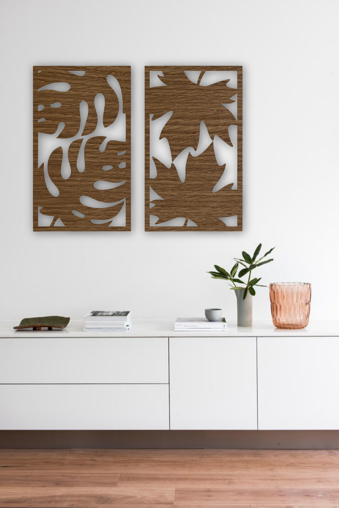 Set of two modern wooden wall art panels with leaf cutout designs displayed above a rattan console table in a cozy living room setting.