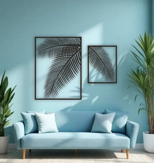 Two-piece black wooden palm leaf wall art set mounted on a blue wall above a modern blue sofa with indoor tropical plants.