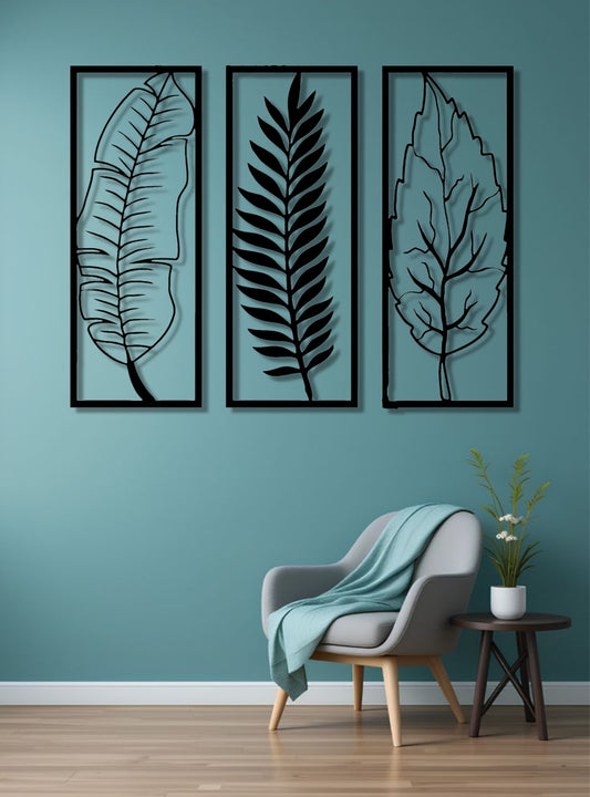 Set of three vertical wooden wall art panels in black finish featuring tropical leaves, mounted above a modern grey sofa in a minimalist living room