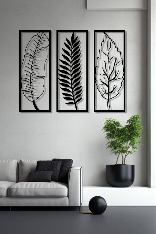 Set of three vertical wooden wall art panels in black finish featuring tropical leaves, mounted above a modern grey sofa in a minimalist living room