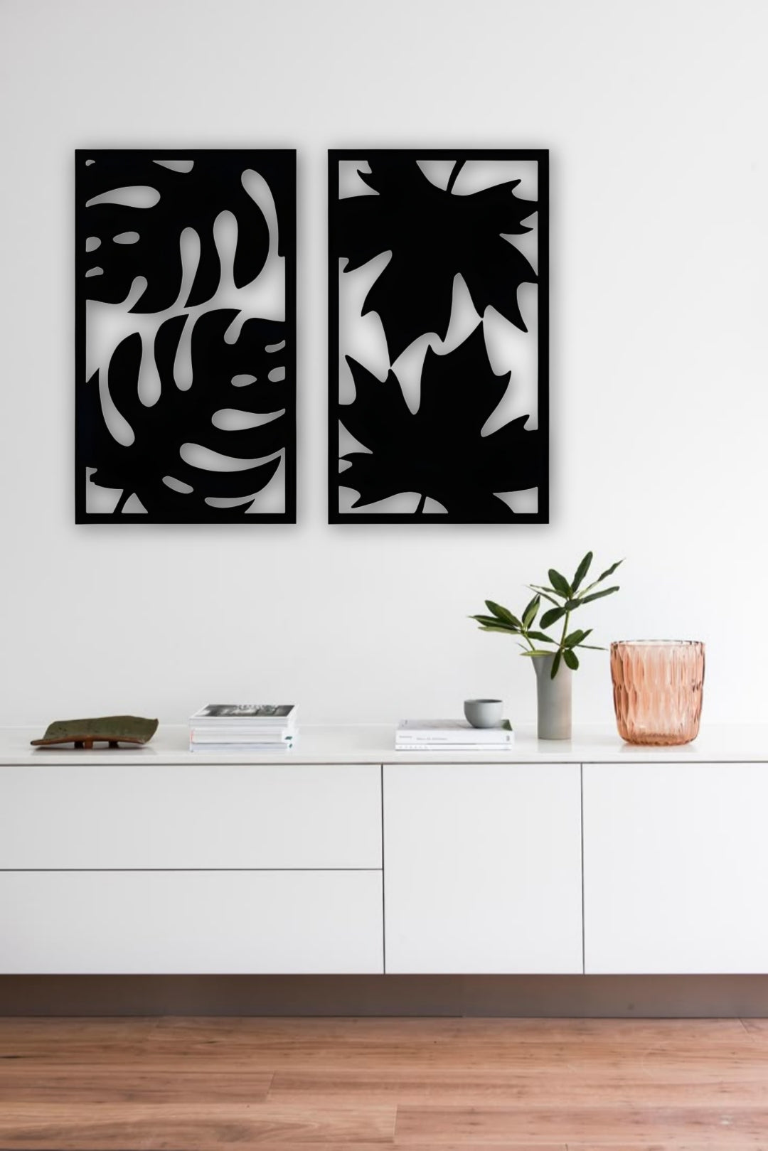 Set of two modern wooden wall art panels with leaf cutout designs displayed above a rattan console table in a cozy living room setting.