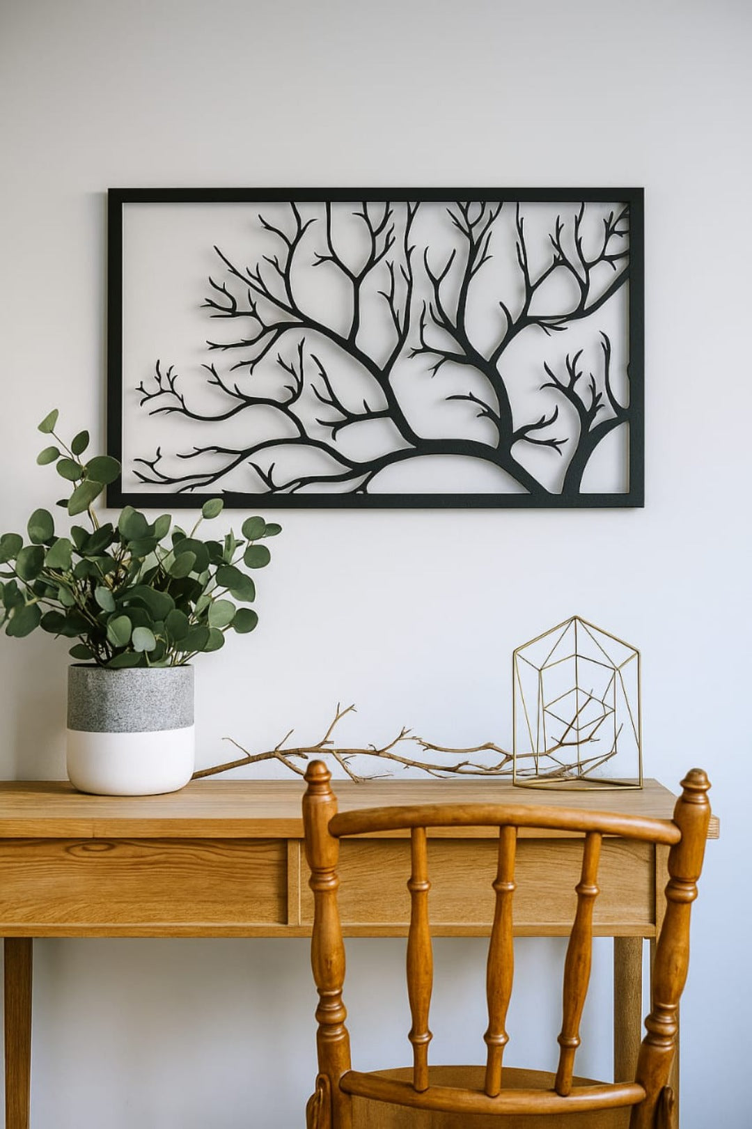 Wooden desk with chair, potted plant, and decorative items against a white wall with framed artwork.