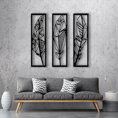 Modern black wooden wall art featuring a set of three vertical panels with abstract geometric feather designs, mounted on a light grey textured wall above a grey sofa.