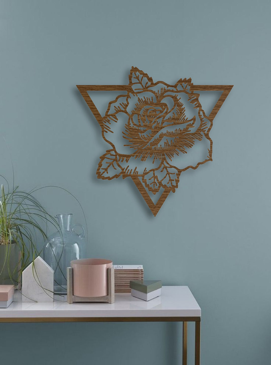 Geometric rose wall art in natural wood brown finish, mounted on a teal wall with decorative table accents in a modern interior.