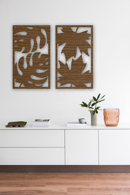 Set of two modern wooden wall art panels with leaf cutout designs displayed above a rattan console table in a cozy living room setting.