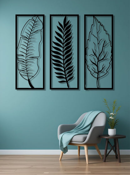 Set of three vertical wooden wall art panels in black finish featuring tropical leaves, mounted above a modern grey sofa in a minimalist living room