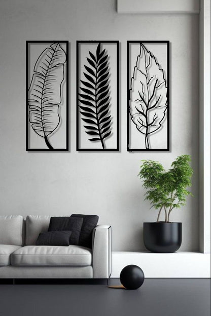 Set of three vertical wooden wall art panels in black finish featuring tropical leaves, mounted above a modern grey sofa in a minimalist living room